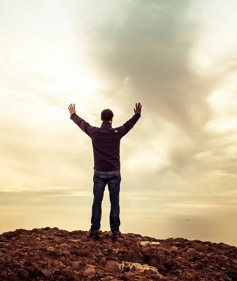 Men's Retreat 2026 · man with arms raised on a rocky summit